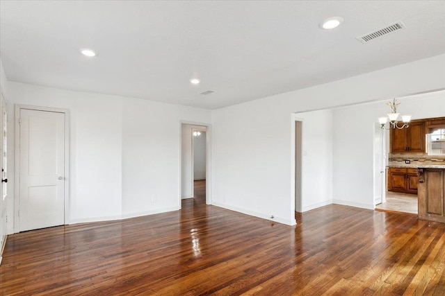 unfurnished living room with an inviting chandelier and dark hardwood / wood-style flooring