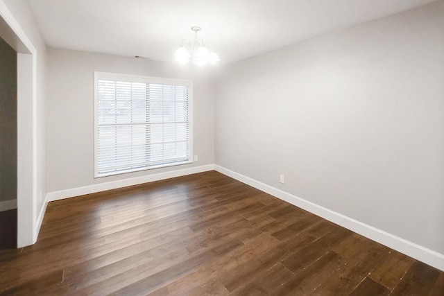 empty room with a notable chandelier and dark hardwood / wood-style floors