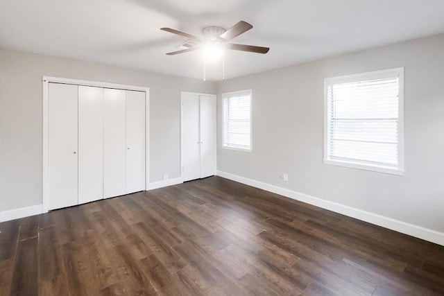 unfurnished bedroom featuring ceiling fan, dark hardwood / wood-style floors, and multiple closets