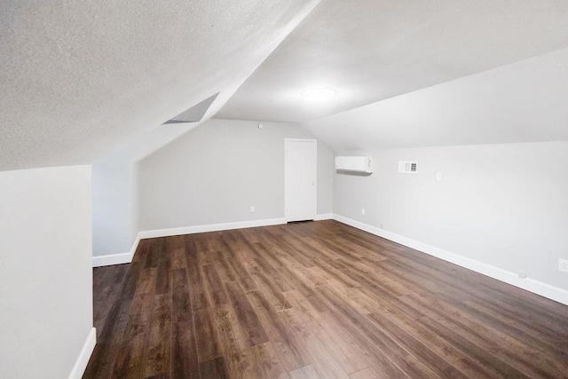 additional living space with an AC wall unit, dark wood-type flooring, a textured ceiling, and vaulted ceiling