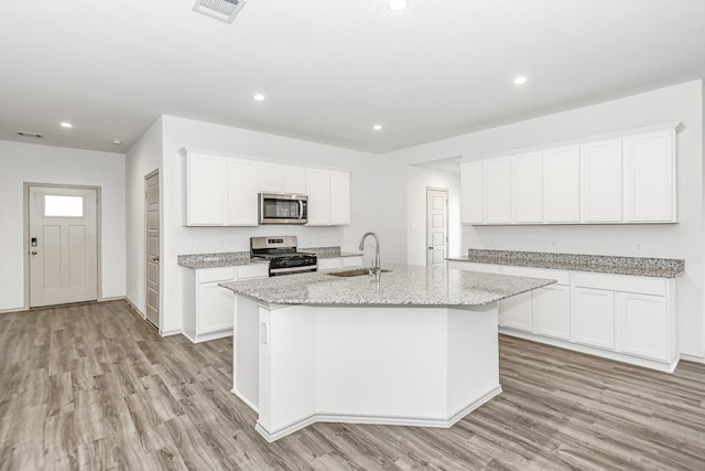 kitchen with white cabinetry, sink, stainless steel appliances, light stone counters, and a center island with sink