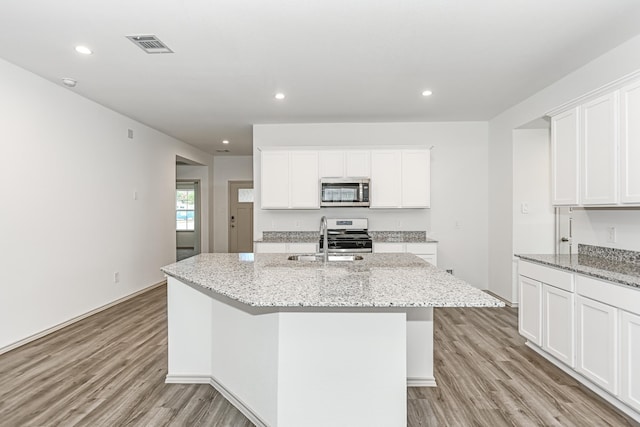 kitchen featuring light stone countertops, sink, white cabinetry, stainless steel appliances, and a kitchen island with sink