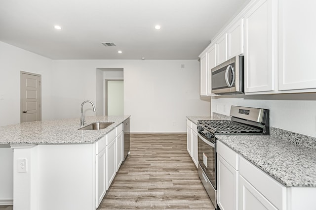 kitchen with appliances with stainless steel finishes, light stone counters, a kitchen island with sink, sink, and white cabinetry