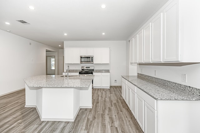 kitchen with sink, an island with sink, light stone counters, white cabinetry, and stainless steel appliances