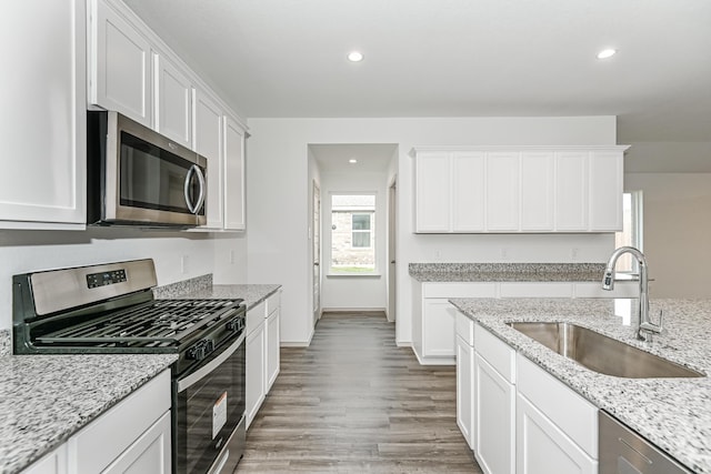 kitchen featuring appliances with stainless steel finishes, white cabinetry, light stone counters, and sink