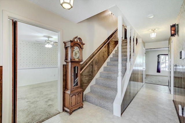 stairs with ceiling fan, carpet, and a textured ceiling