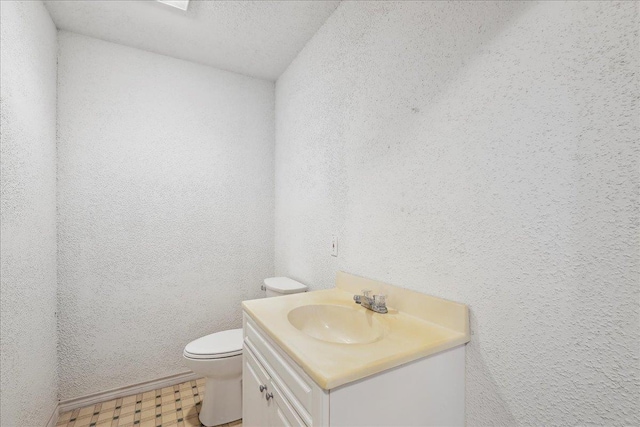 half bath with a textured wall, vanity, toilet, and tile patterned floors