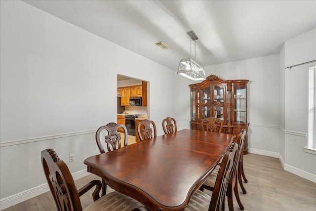 dining space with light wood-type flooring, visible vents, and baseboards