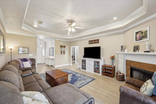 living area featuring a brick fireplace, a raised ceiling, visible vents, and light wood-style floors