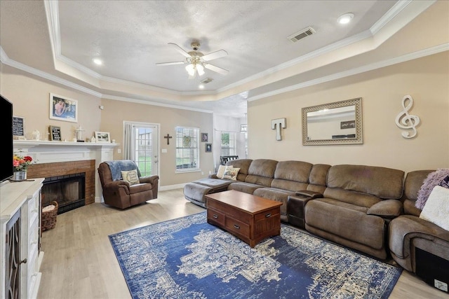 living room featuring visible vents, ornamental molding, light wood-type flooring, a brick fireplace, and a raised ceiling