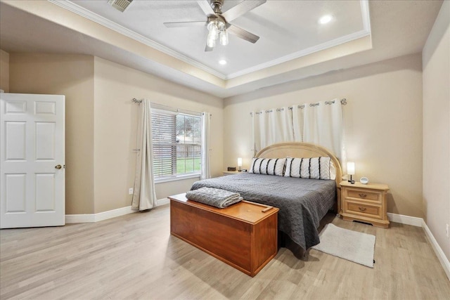 bedroom with light wood-style floors, a tray ceiling, crown molding, and baseboards