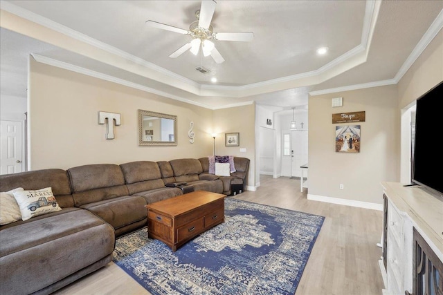 living area featuring baseboards, ceiling fan, a tray ceiling, crown molding, and light wood-type flooring