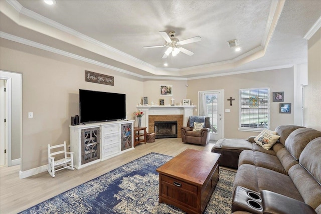 living room featuring visible vents, a tray ceiling, light wood-style flooring, and ornamental molding