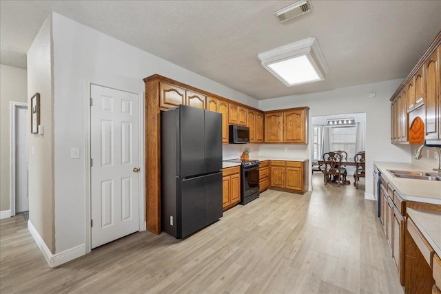 kitchen featuring light wood-style flooring, a sink, visible vents, black appliances, and brown cabinetry