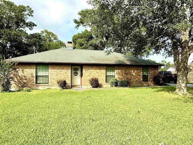 single story home with roof with shingles, a chimney, brick siding, and a front yard