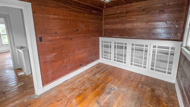 empty room featuring wood-type flooring, radiator heating unit, and wood walls