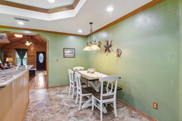 dining area featuring ceiling fan, ornamental molding, and wood walls