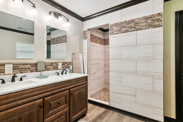 bathroom featuring a tile shower, crown molding, hardwood / wood-style floors, a textured ceiling, and vanity