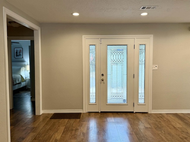 foyer featuring visible vents, dark wood-type flooring, a textured ceiling, recessed lighting, and baseboards