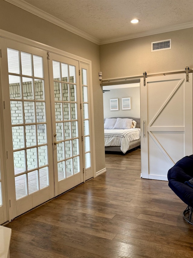 doorway to outside featuring visible vents, a barn door, dark wood-type flooring, and ornamental molding