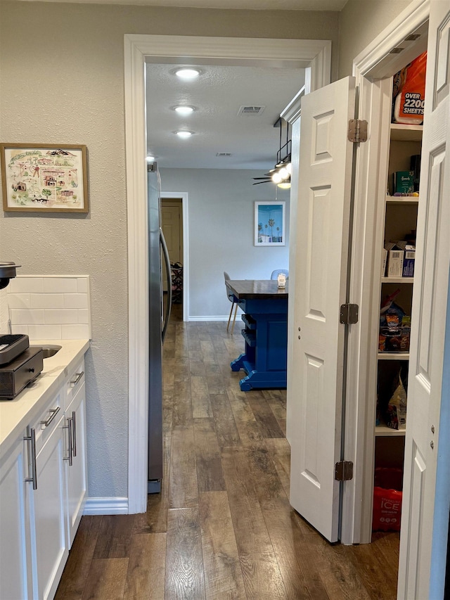 hall with visible vents, dark wood-style flooring, and baseboards