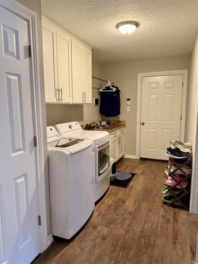 laundry room featuring washing machine and clothes dryer, dark wood-style flooring, cabinet space, a textured ceiling, and a sink