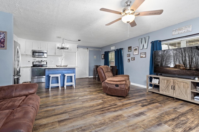 living area with a ceiling fan, a textured ceiling, dark wood finished floors, a barn door, and baseboards