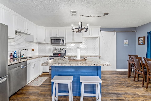 kitchen with visible vents, a sink, a barn door, appliances with stainless steel finishes, and dark wood-style flooring