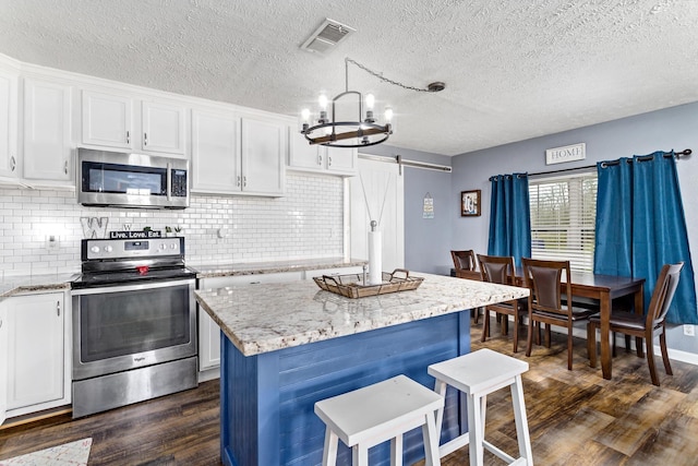 kitchen with visible vents, a barn door, stainless steel appliances, dark wood-style floors, and white cabinetry