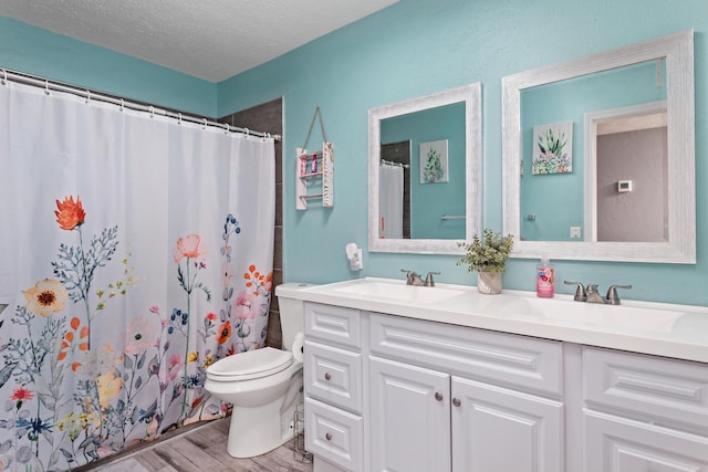 full bathroom with toilet, double vanity, wood finished floors, a textured ceiling, and a sink