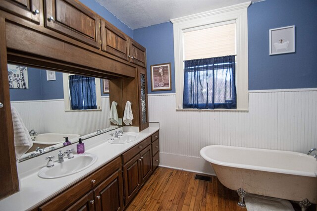 2108 Harrison Ave, Beaumont, TX 77701 - full bathroom with a wainscoted wall, a freestanding tub, wood finished floors, double vanity, and a textured ceiling