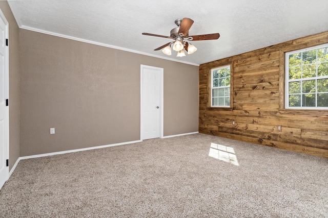 carpeted spare room with a textured ceiling, ceiling fan, crown molding, and wood walls