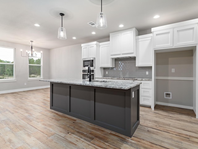 kitchen with backsplash, white cabinets, light wood-style flooring, and a sink