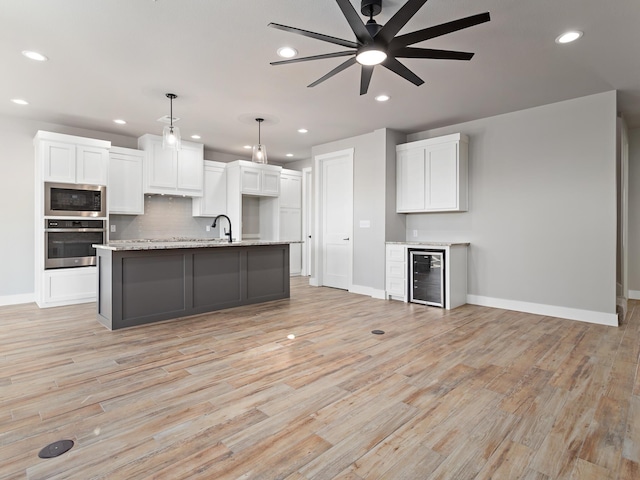kitchen with beverage cooler, appliances with stainless steel finishes, white cabinetry, light wood-type flooring, and backsplash