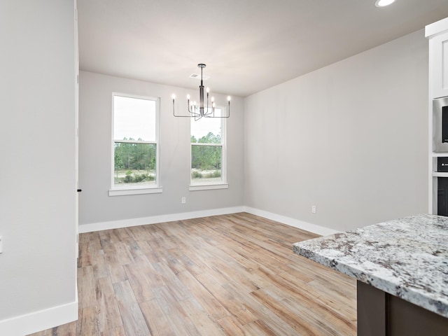 unfurnished dining area featuring an inviting chandelier, light wood-style flooring, and baseboards