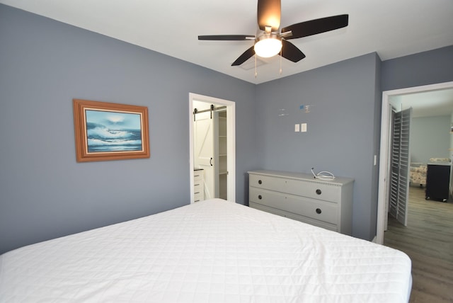 bedroom with hardwood / wood-style floors, a barn door, and ceiling fan