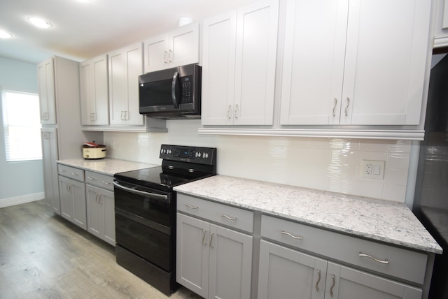 kitchen featuring gray cabinetry, electric range, light stone counters, and light wood-type flooring