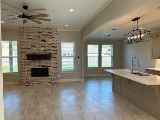 kitchen featuring sink, a brick fireplace, decorative light fixtures, a center island with sink, and ceiling fan with notable chandelier