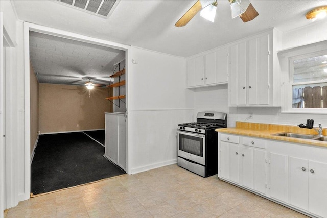 kitchen with backsplash, sink, gas range, ceiling fan, and white cabinetry