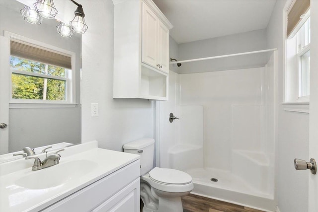 bathroom with a notable chandelier, toilet, hardwood / wood-style flooring, walk in shower, and vanity