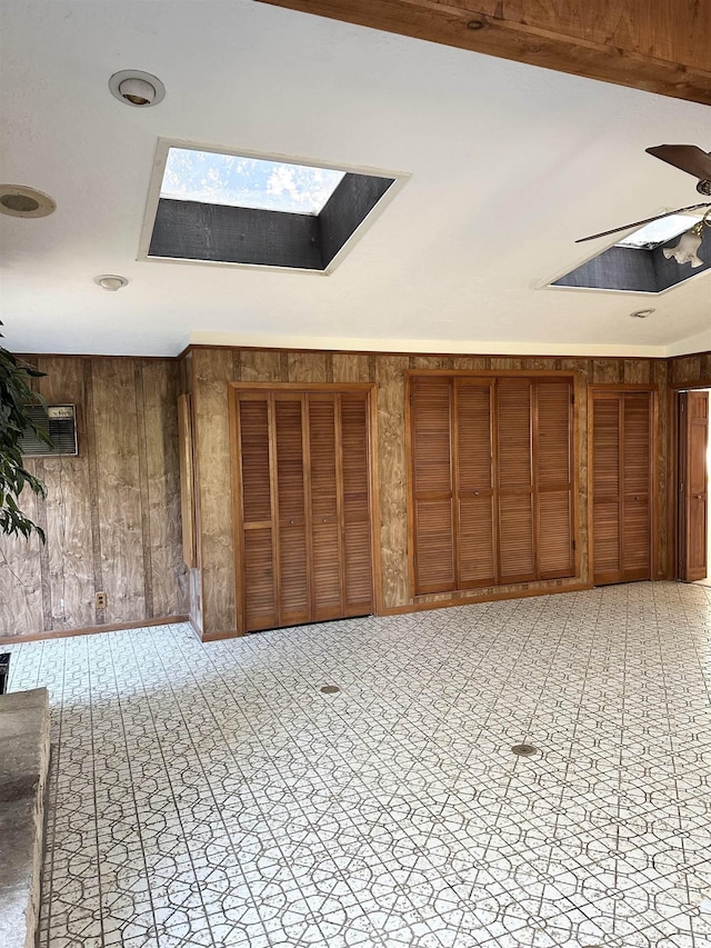 interior space with a skylight, wooden walls, and ceiling fan