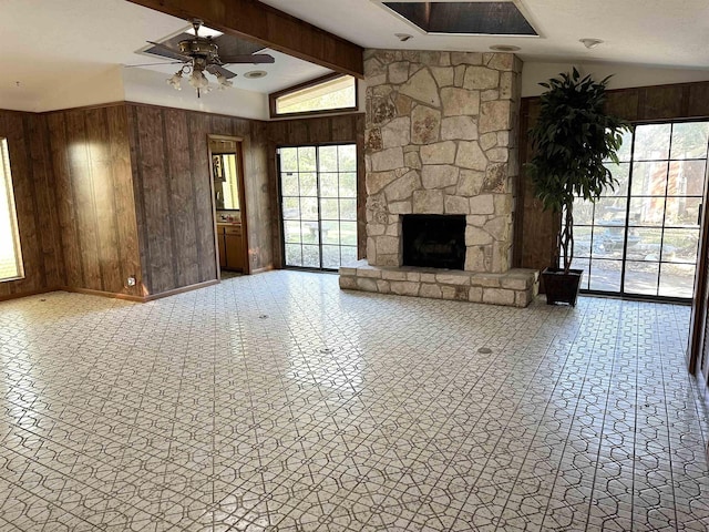 unfurnished living room with vaulted ceiling with beams, ceiling fan, a stone fireplace, and wooden walls