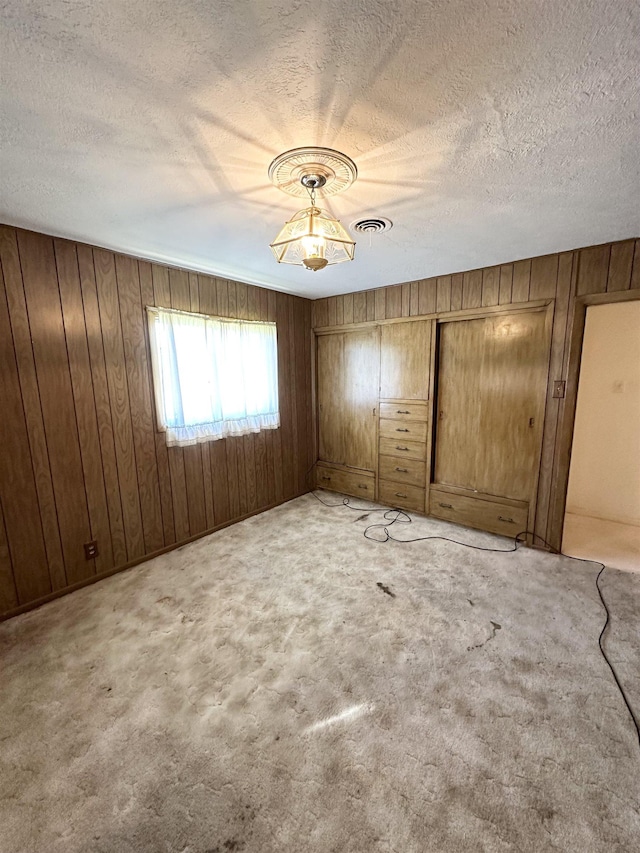 unfurnished bedroom with carpet, a textured ceiling, and wooden walls