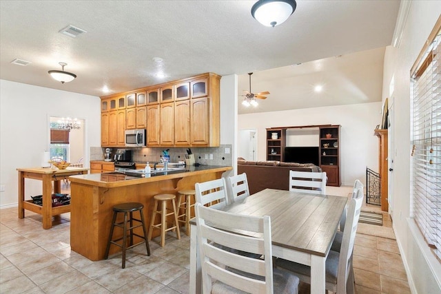 kitchen featuring a kitchen breakfast bar, ceiling fan, tasteful backsplash, light tile patterned flooring, and kitchen peninsula