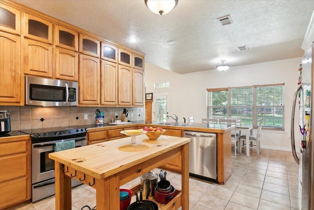 kitchen with sink, decorative backsplash, a textured ceiling, appliances with stainless steel finishes, and light tile patterned flooring