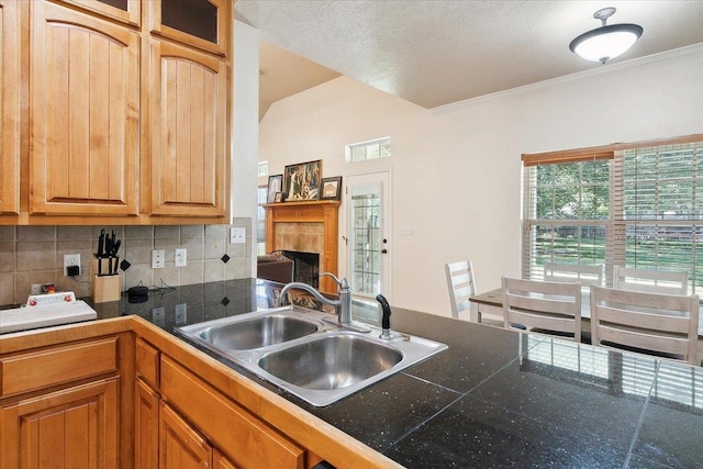 kitchen featuring backsplash, sink, ornamental molding, kitchen peninsula, and a tiled fireplace