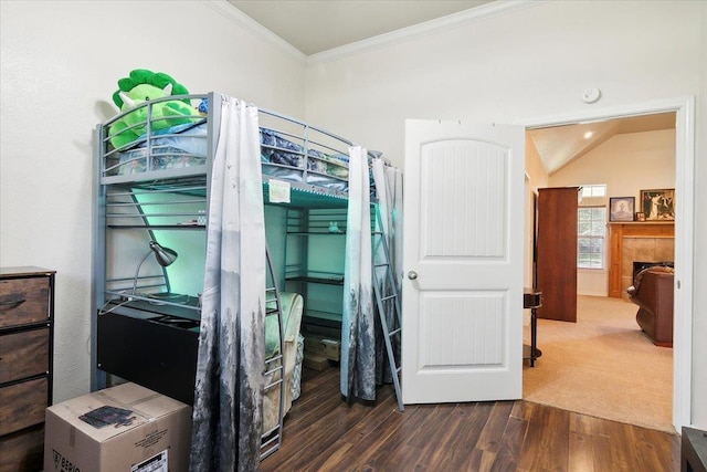 bedroom featuring dark wood-type flooring, vaulted ceiling, crown molding, and a tiled fireplace