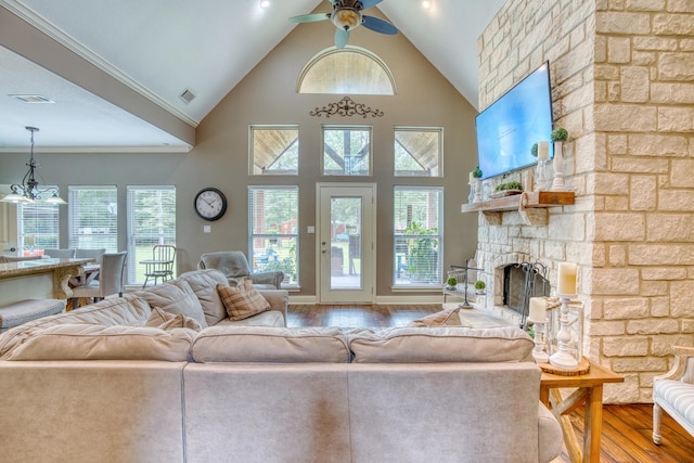 living room featuring hardwood / wood-style floors, ceiling fan with notable chandelier, ornamental molding, a fireplace, and a healthy amount of sunlight