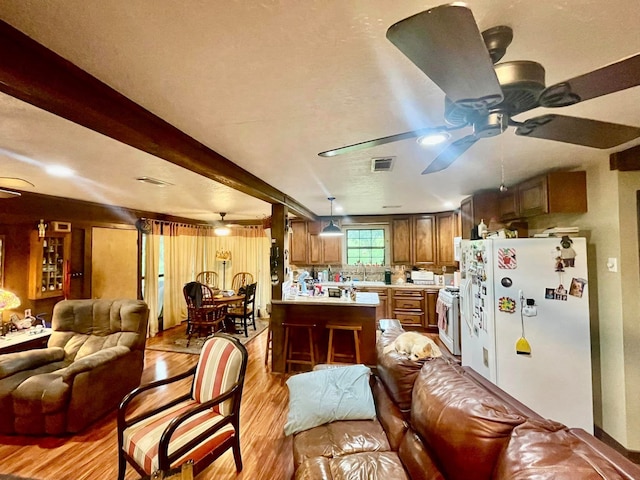 kitchen featuring beamed ceiling, kitchen peninsula, pendant lighting, white appliances, and light wood-type flooring