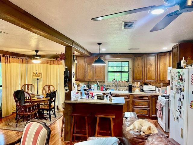 kitchen featuring a kitchen breakfast bar, light hardwood / wood-style flooring, pendant lighting, a textured ceiling, and white appliances